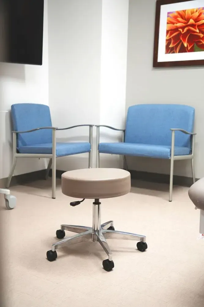 Light blue chairs and a rolling stool in a corner of a medical exam room.