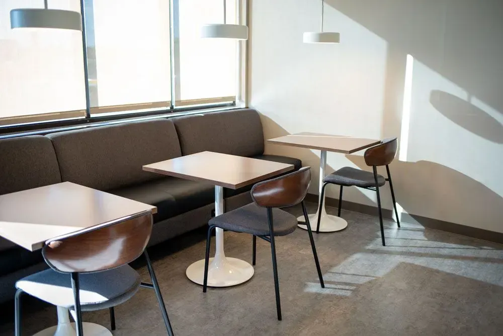 Cozy cafe seating area: booths, tables, chairs, and overhead lights by a large window.