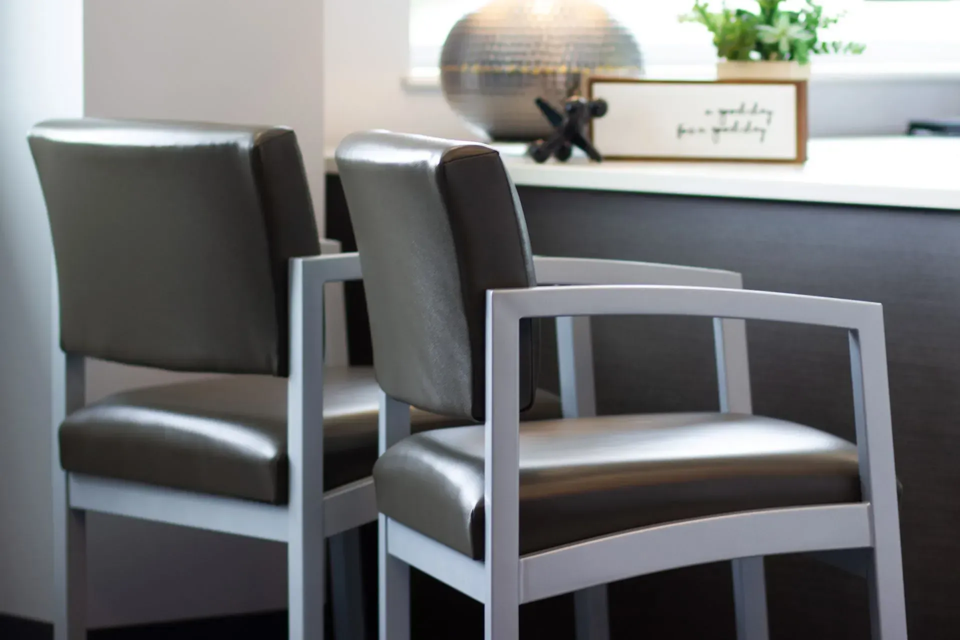 Two gray leather chairs with light gray frames in a waiting area.