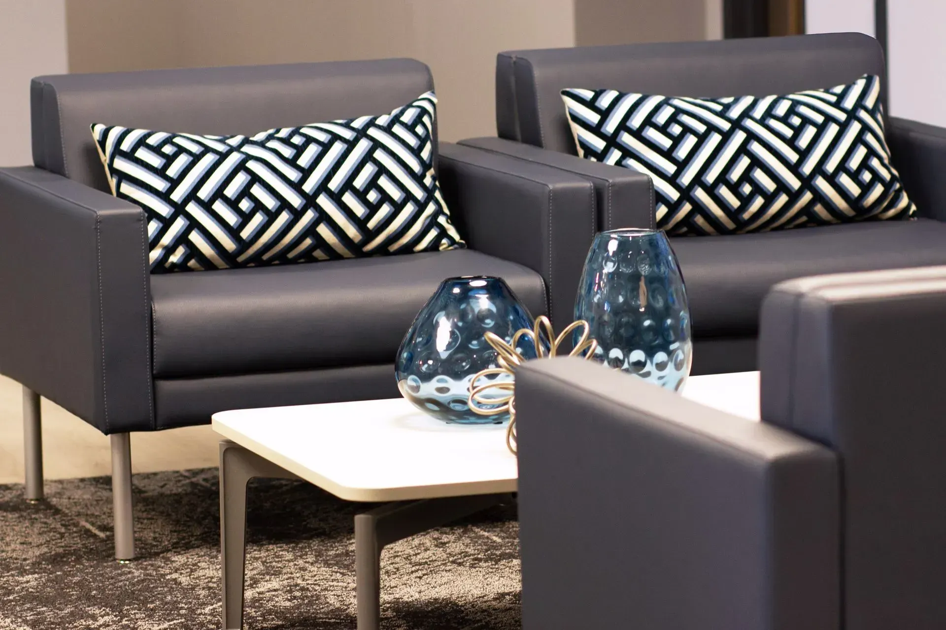 Two gray armchairs with patterned pillows, coffee table with blue vases, and decorative object.
