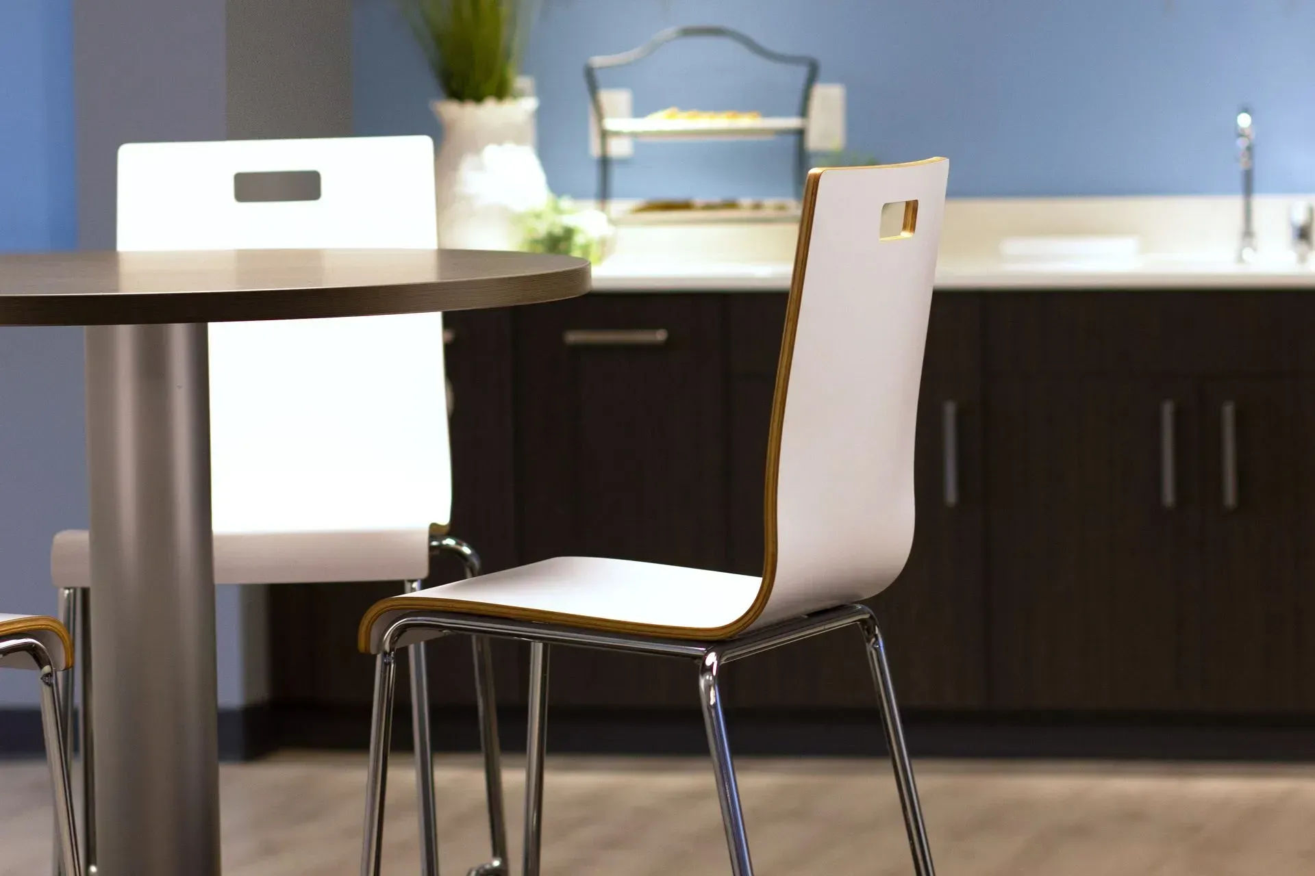 White chair at a round table, dark cabinets and blue wall in the background.