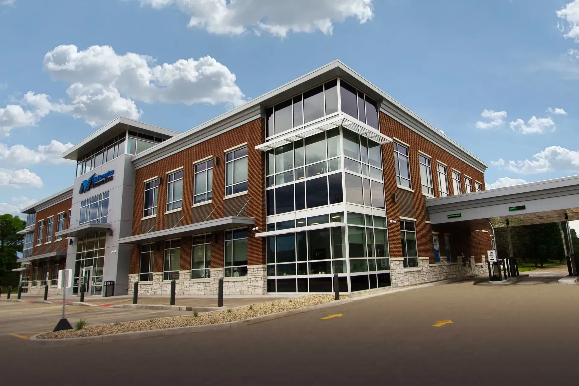 Modern brick and glass bank building with drive-through lane under a blue sky.
