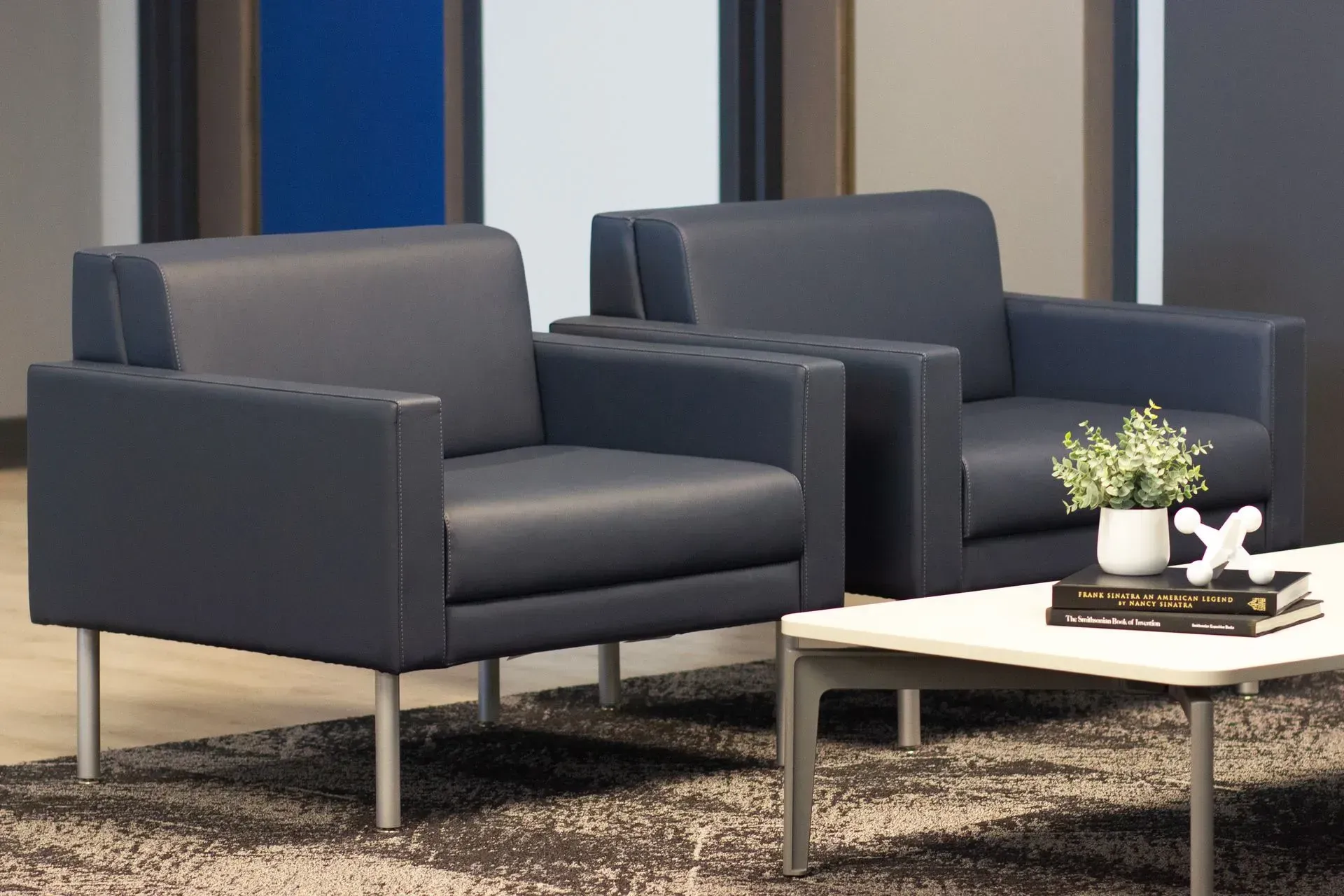 Two navy armchairs with silver legs in an office setting, with a small table and plants.