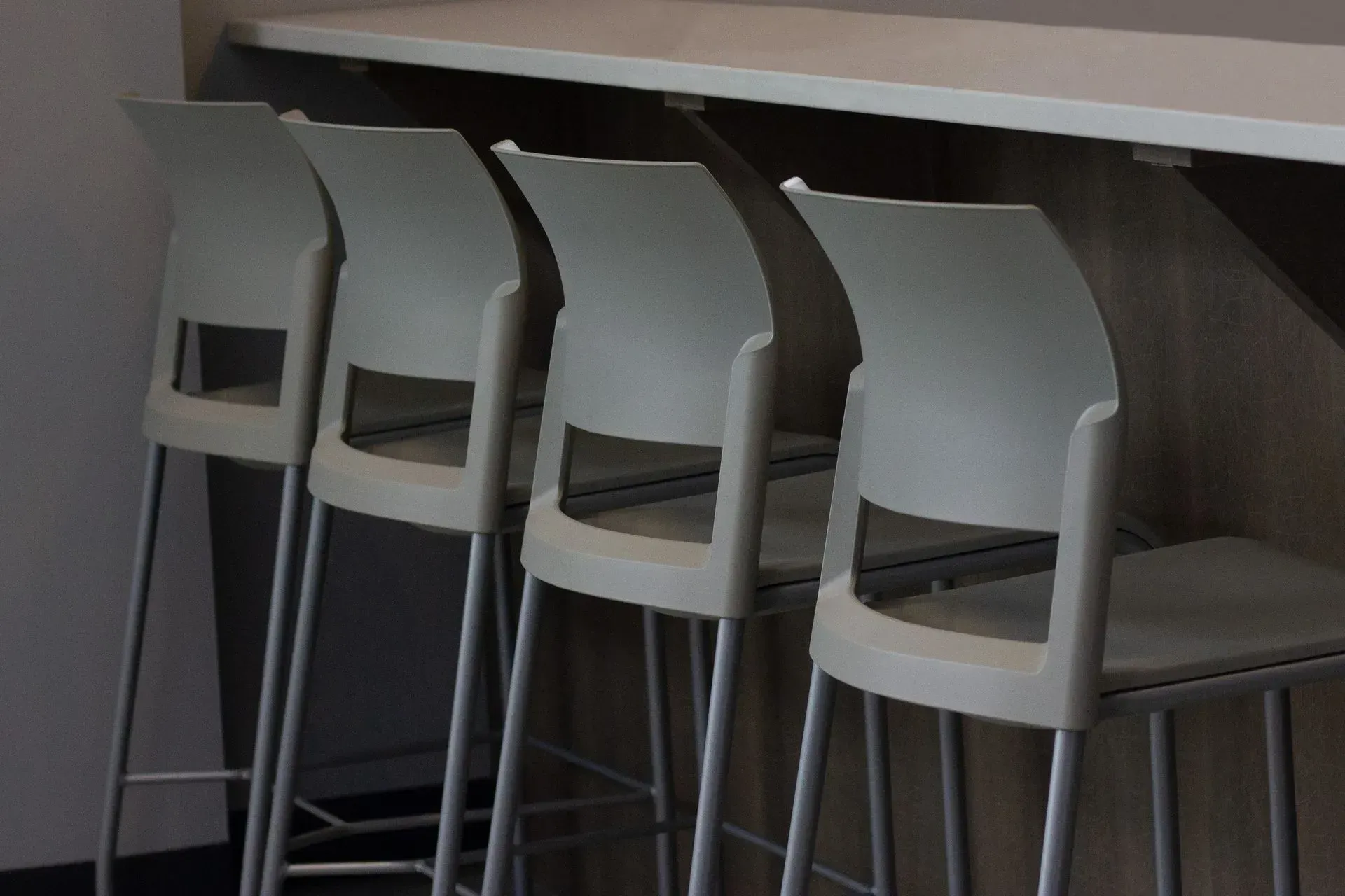 Four white bar stools lined up at a counter.