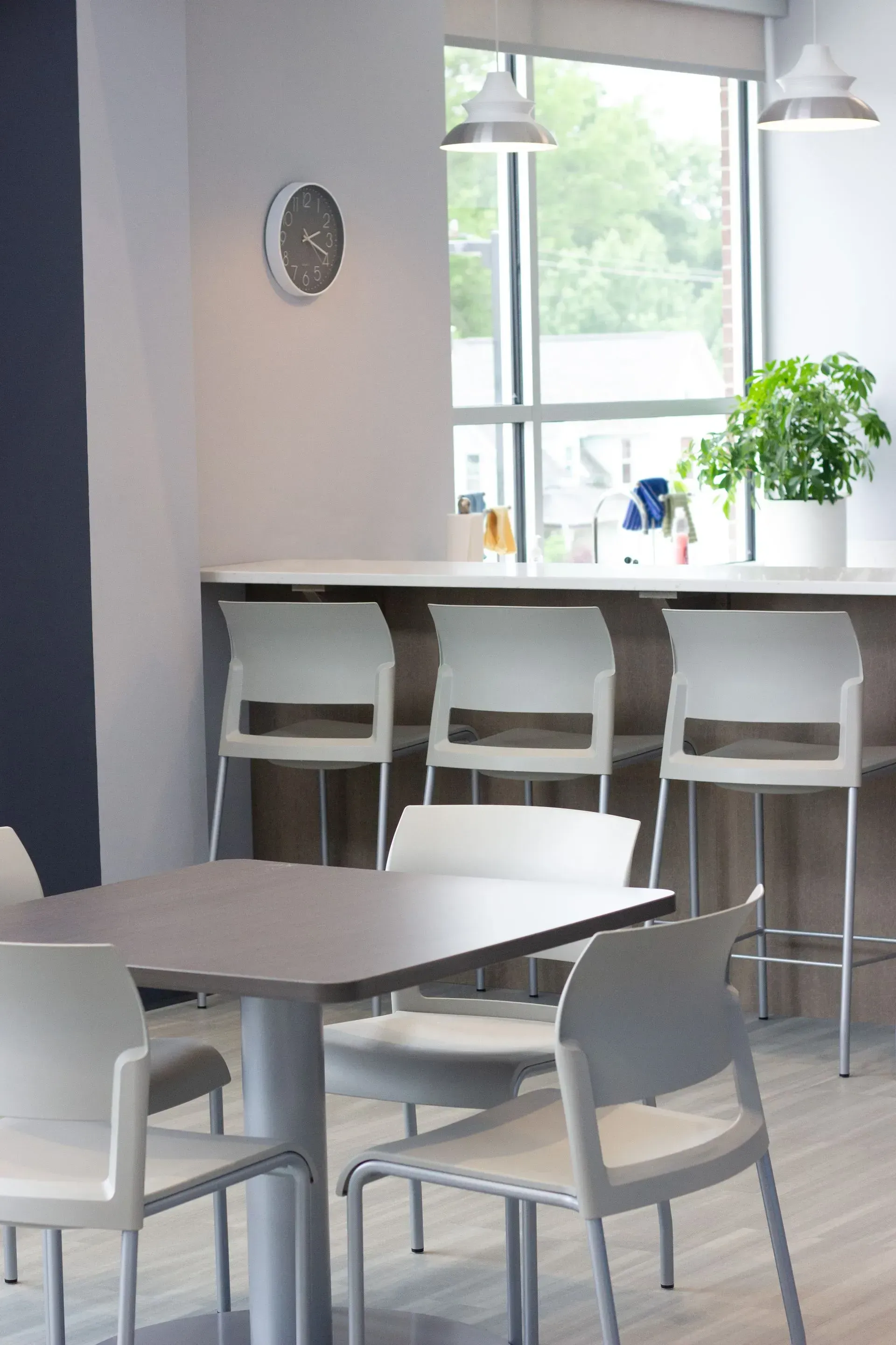 A cafe space with white chairs, a table, and a countertop with bar stools by a window.