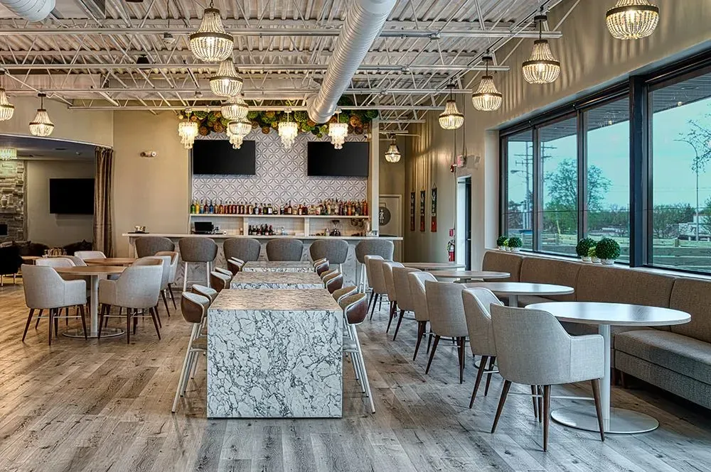 Restaurant interior with tables, bar, decorative lighting, and large windows.