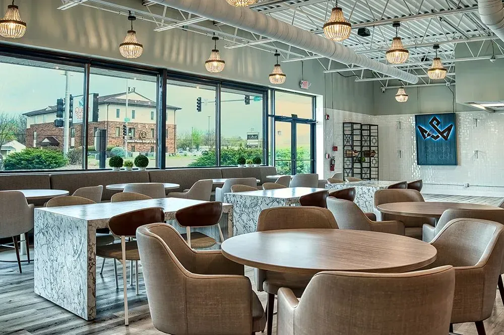 Empty modern restaurant interior with tables, chairs, and large windows offering an exterior view.