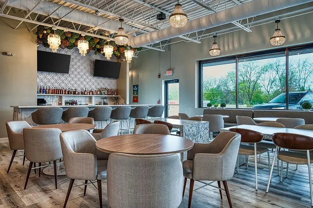 Interior of a restaurant with a bar, tables, chairs, and large windows with outdoor views.
