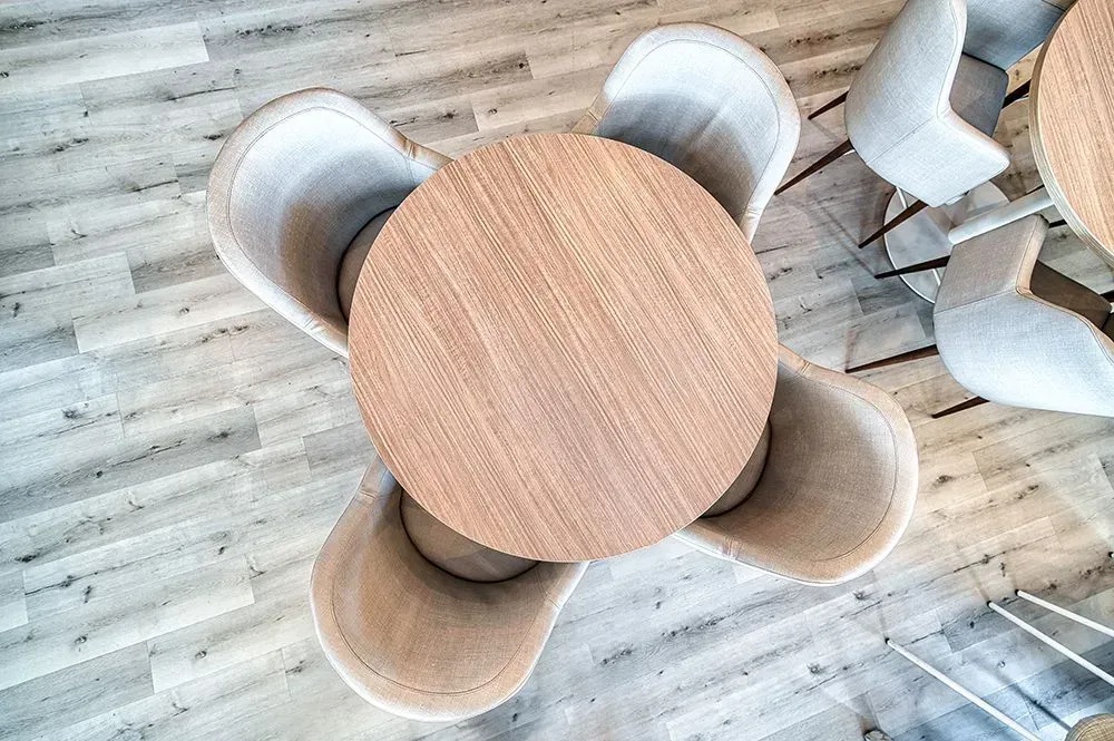 Overhead view of a round wooden table with four beige chairs on a wood-look floor.