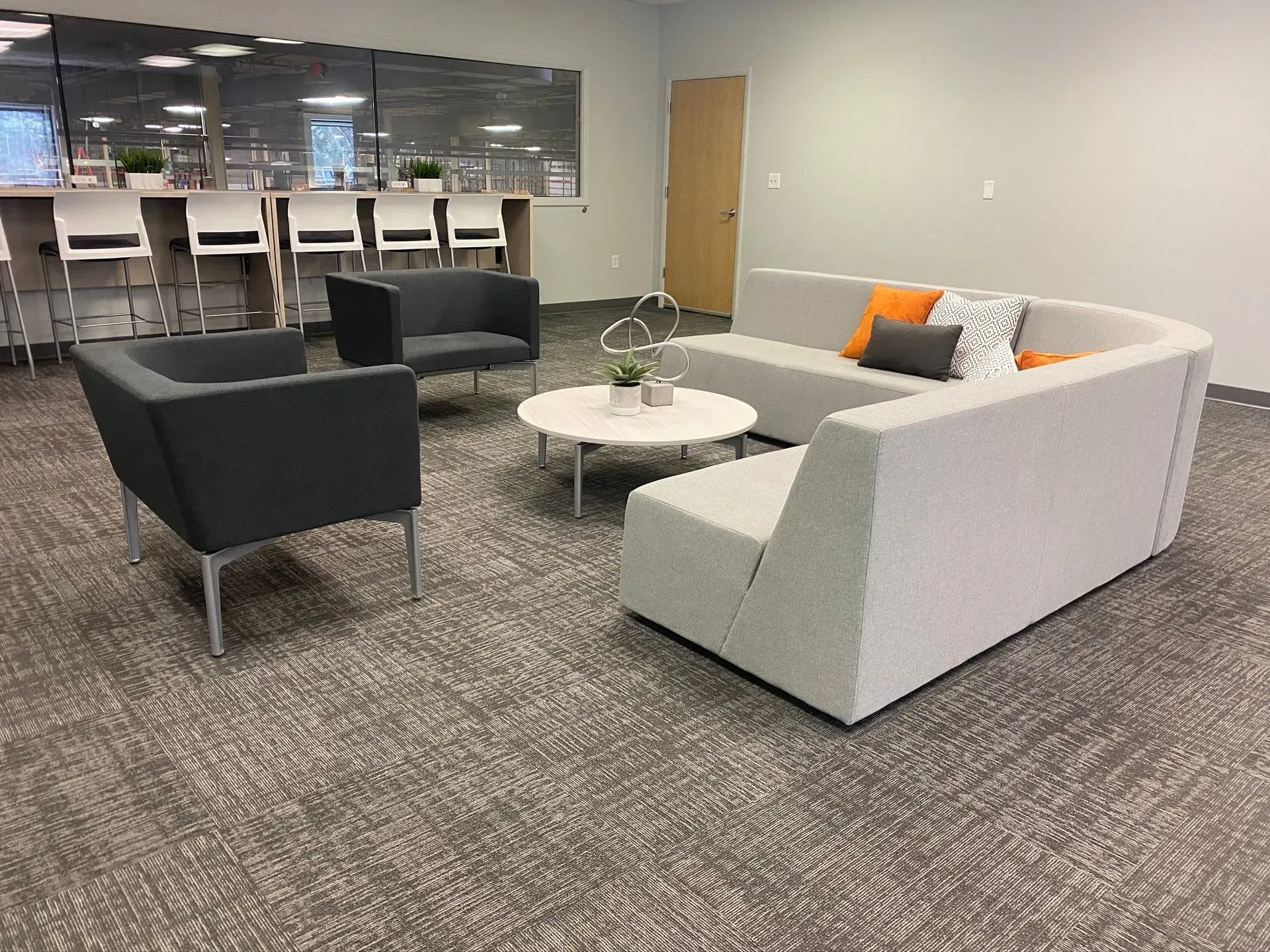Lounge area with gray sofas, small round table, and bar with stools. Gray carpet and neutral walls.