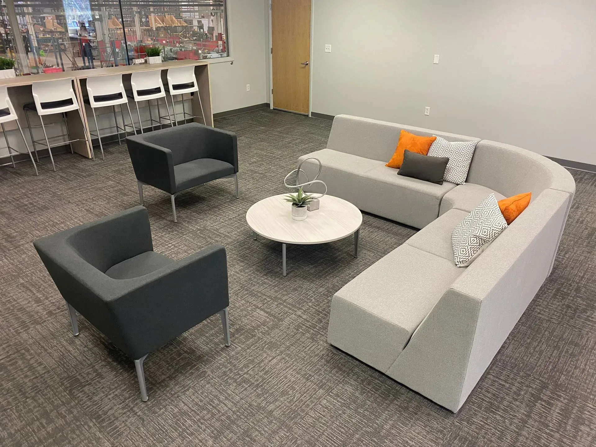 Modern office seating area: curved sofa, two armchairs, round table, neutral colors, office setting.