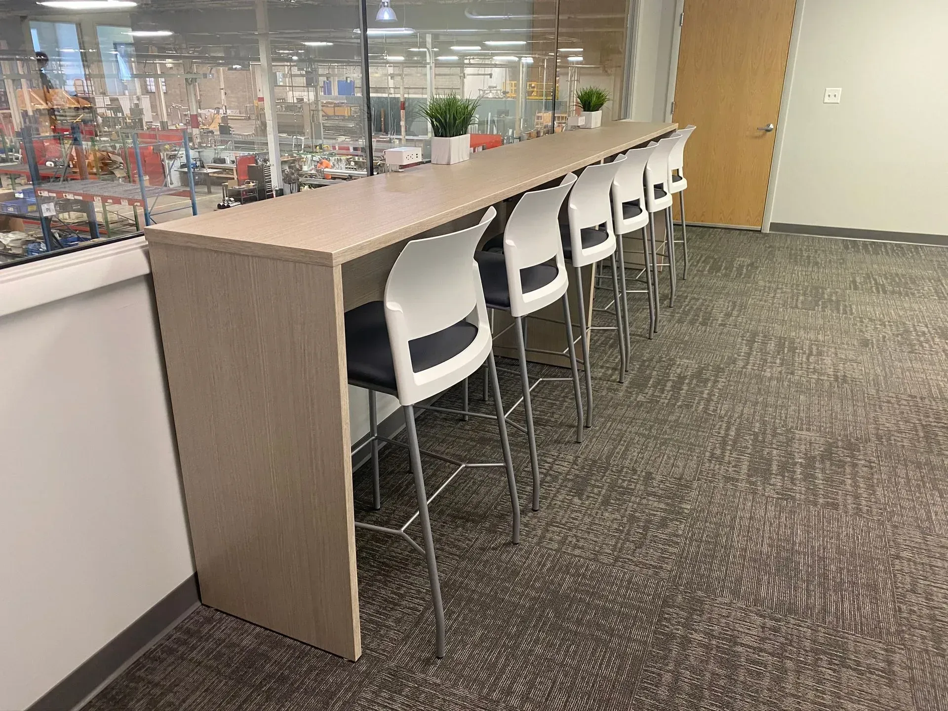 A row of white bar stools at a long, beige counter in an office setting.