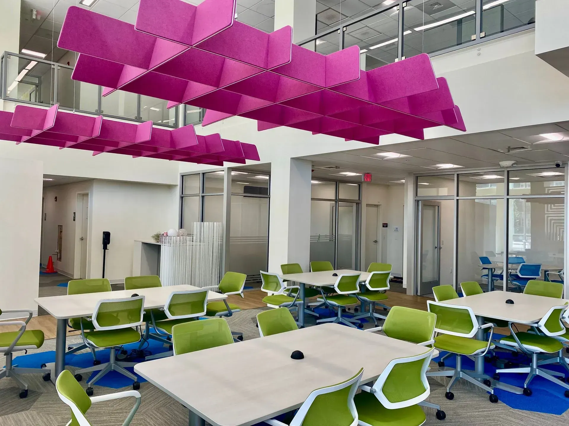 Modern workspace with square tables, green chairs, and pink ceiling panels.