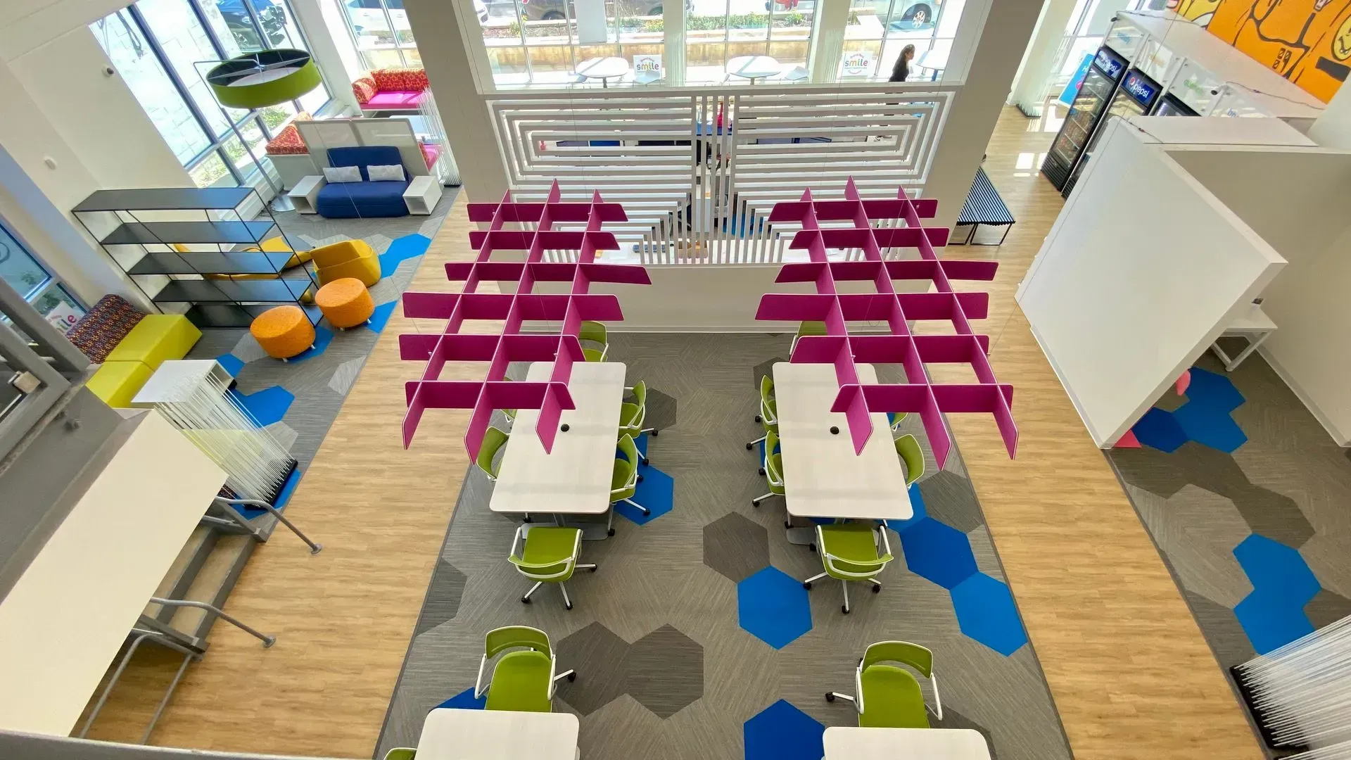 High-angle view of a colorful modern library. Tables with green chairs, geometric carpet, pink ceiling decor.
