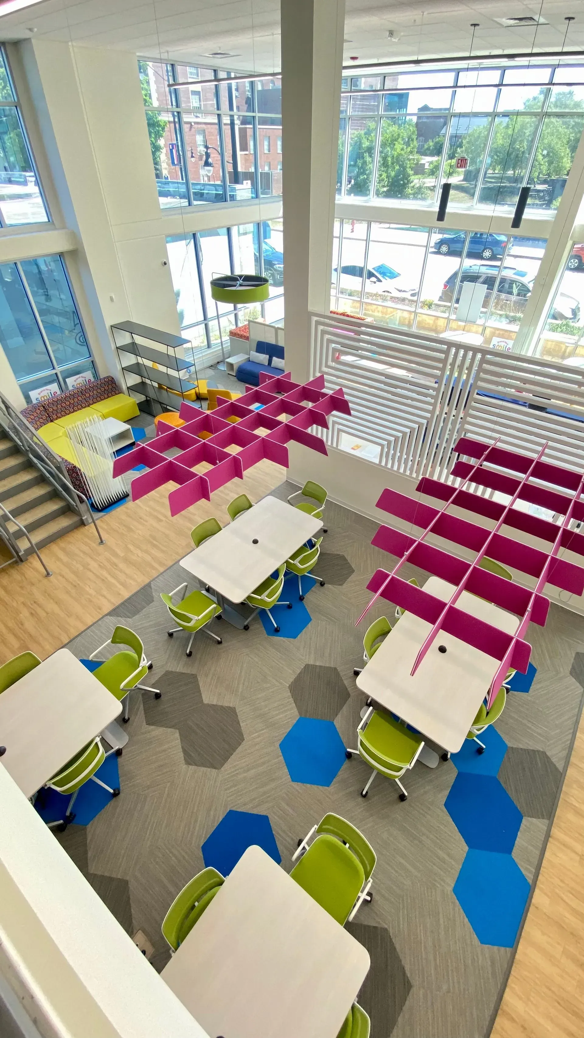 High-angle view of a library with tables, chairs, colorful carpet, and a large window.