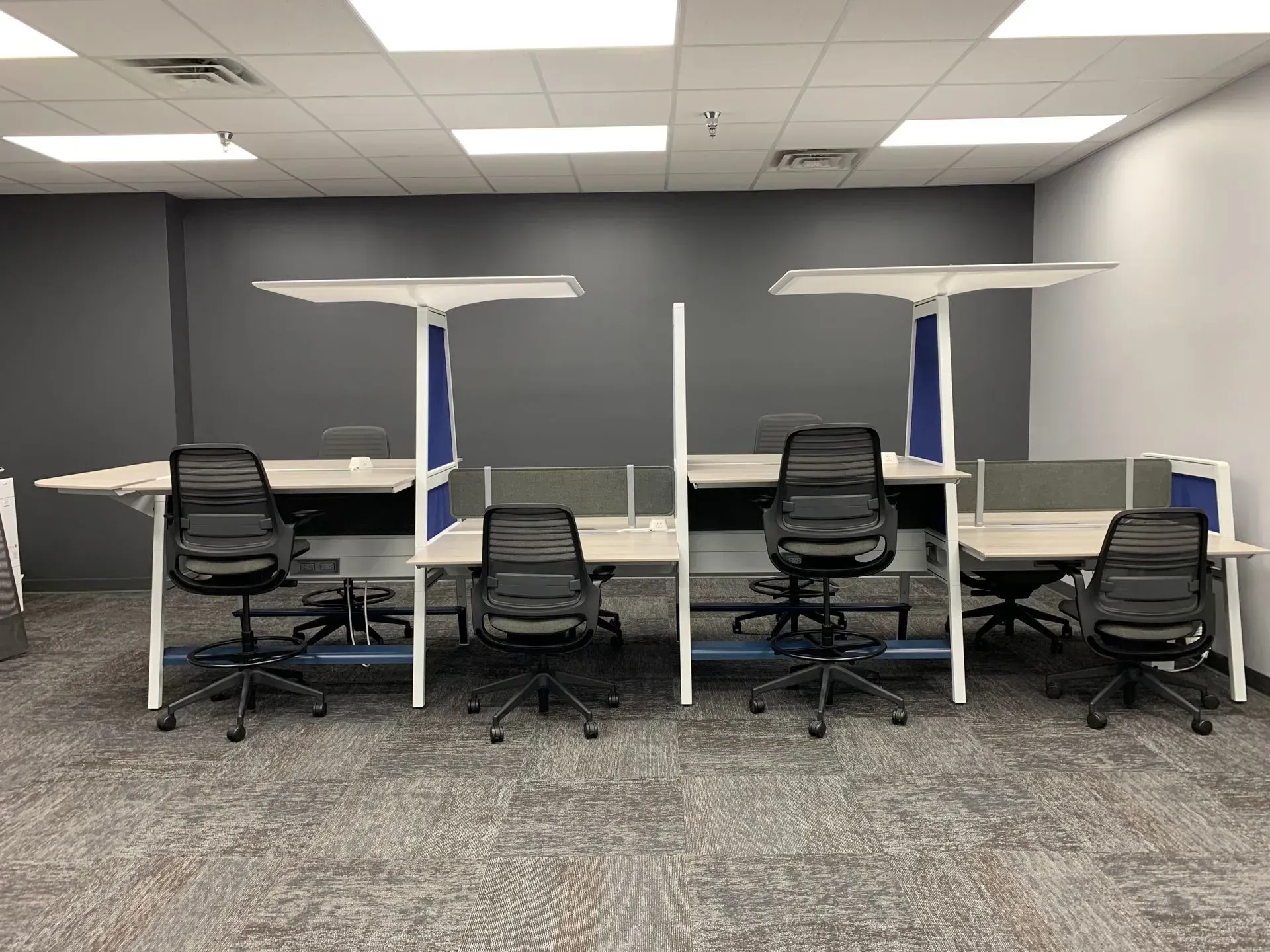 Office cubicles with black rolling chairs, gray dividers, and overhead lights.