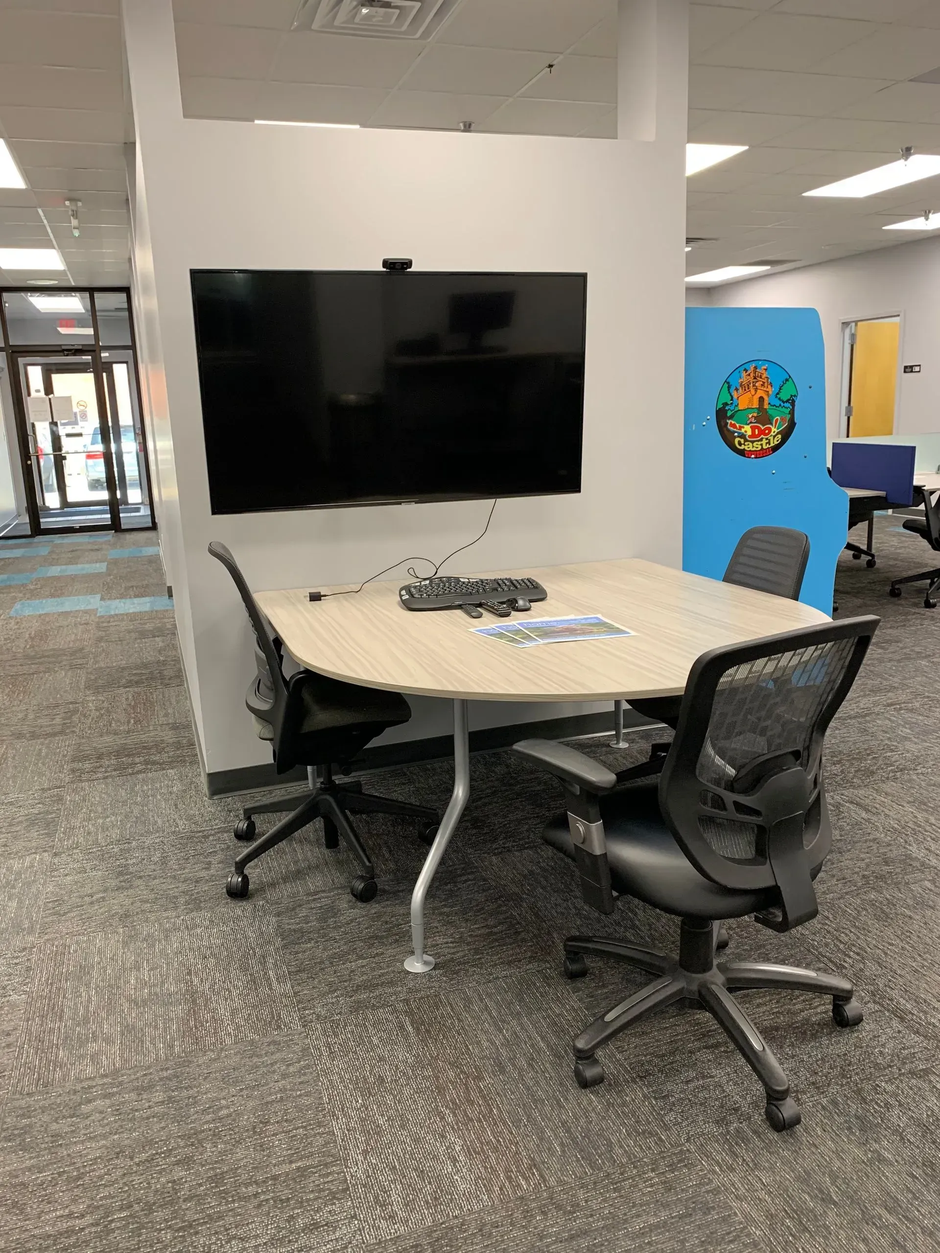 Meeting table with four chairs, mounted TV, and a control panel, in an office setting.