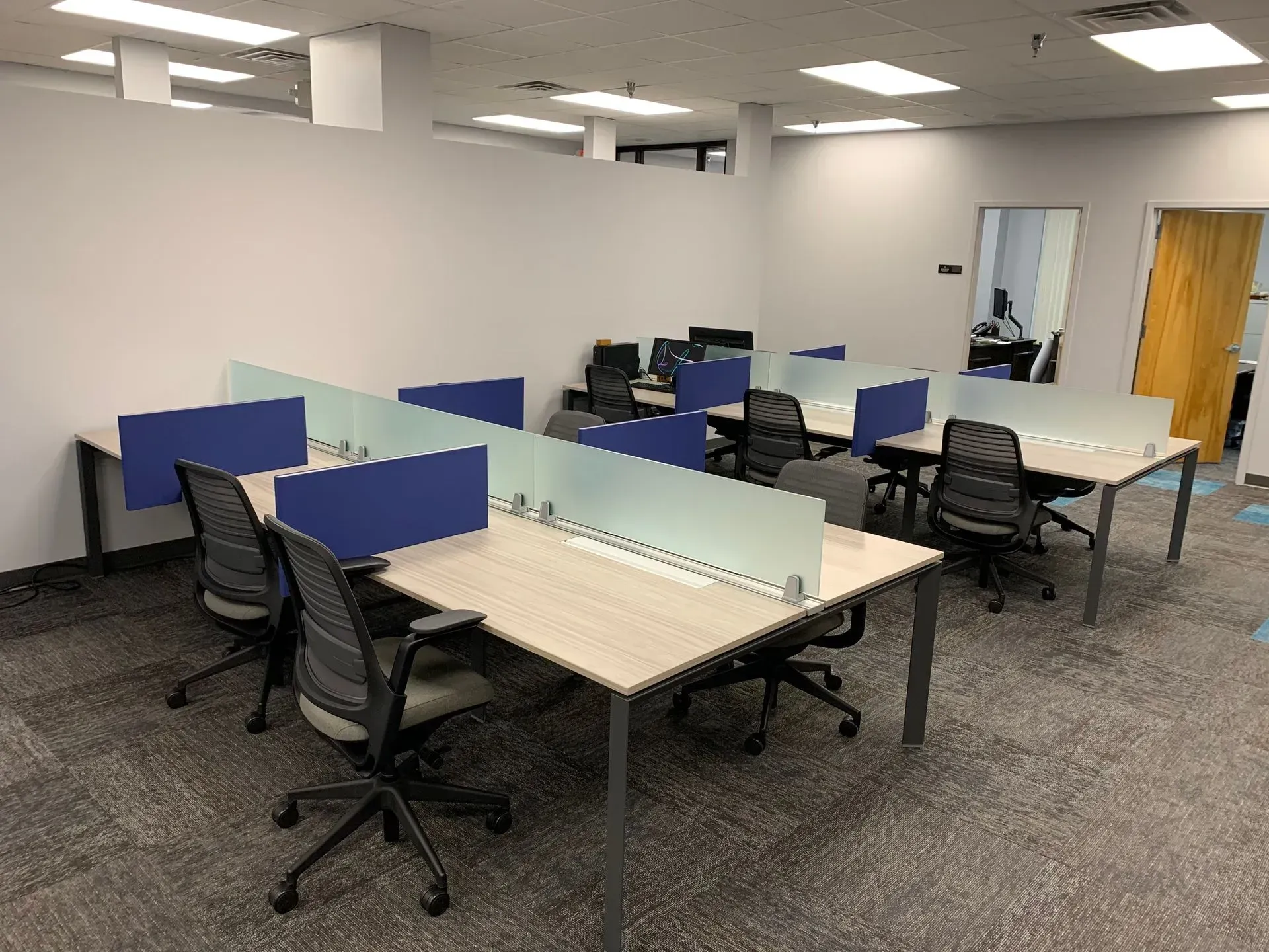 Office space with several desks, chairs, and partitions, gray walls and carpet.