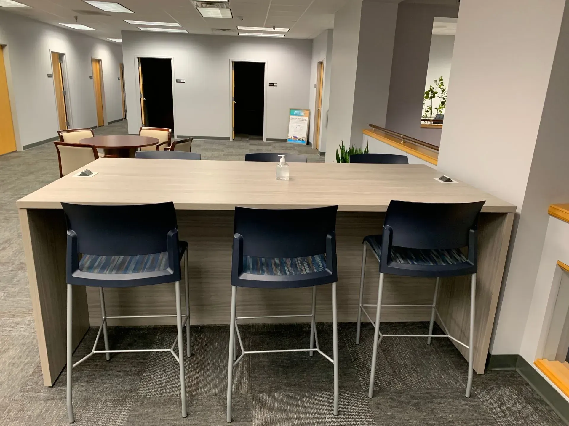 Three black bar stools at a long, light-colored table in an office space.