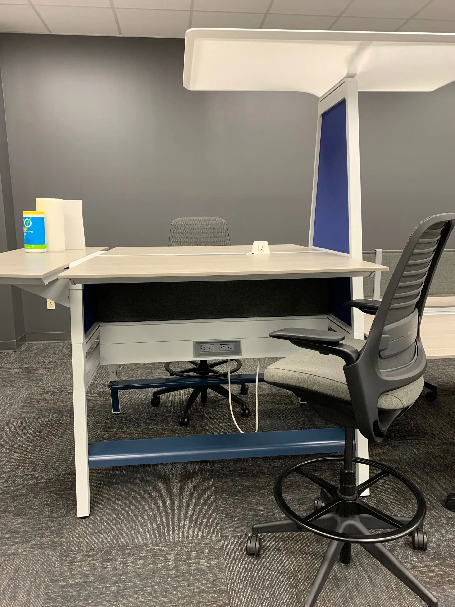 Office desk with a built-in shelf, power outlets, and a drafting chair in a modern office space.