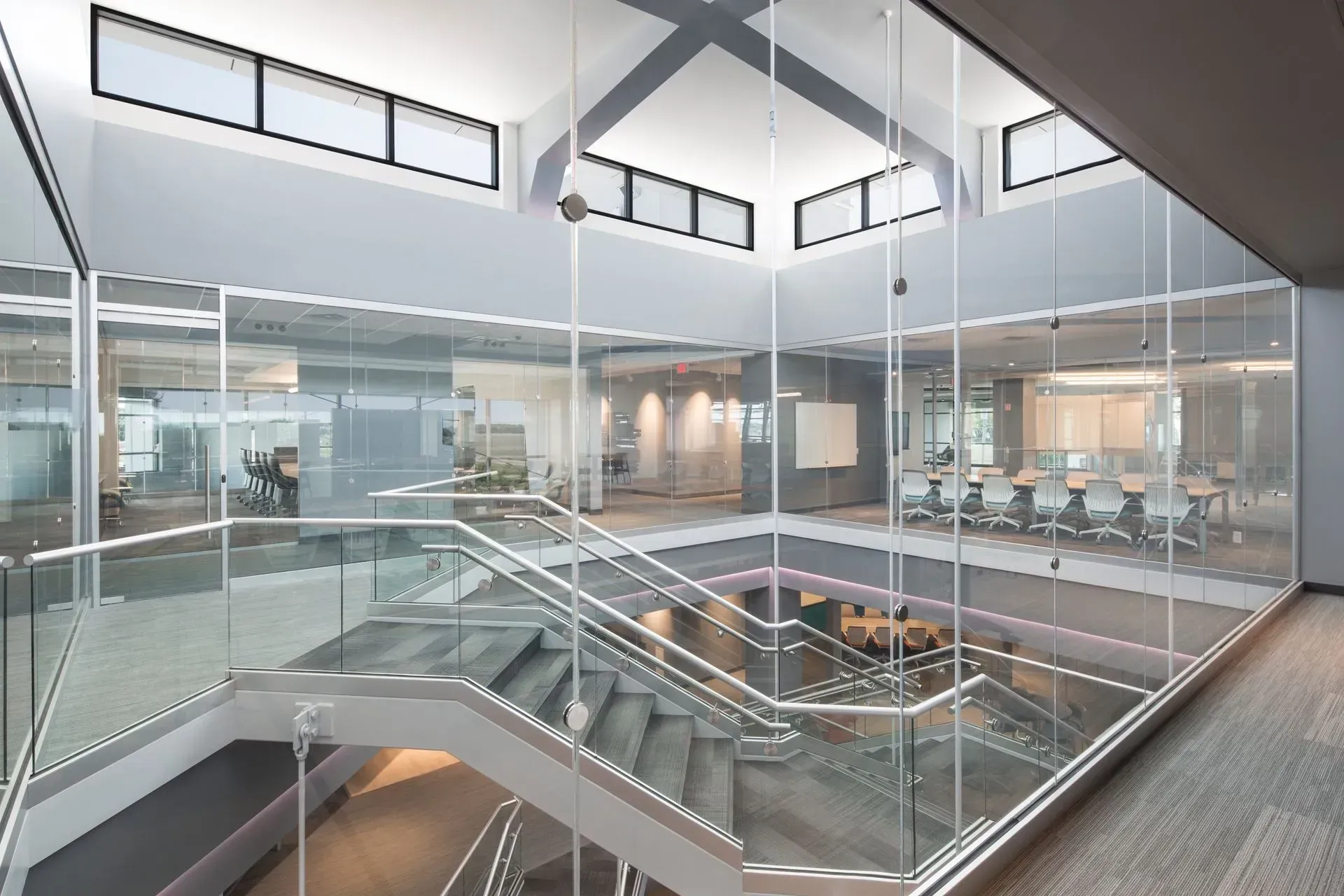 Modern office interior with glass walls, a staircase, and several workspaces visible.