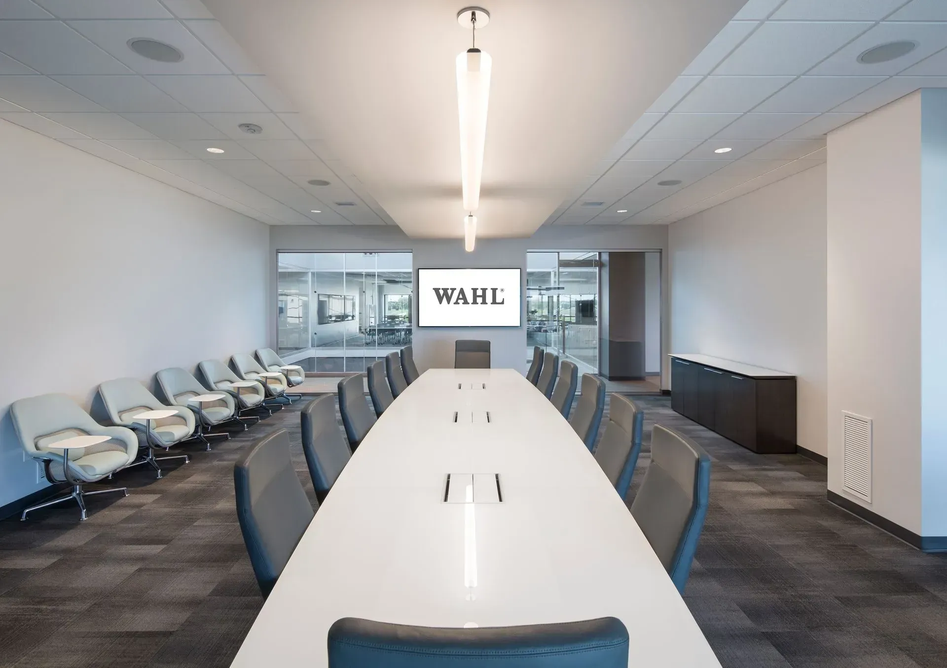 Conference room with long white table, chairs, and a screen displaying 