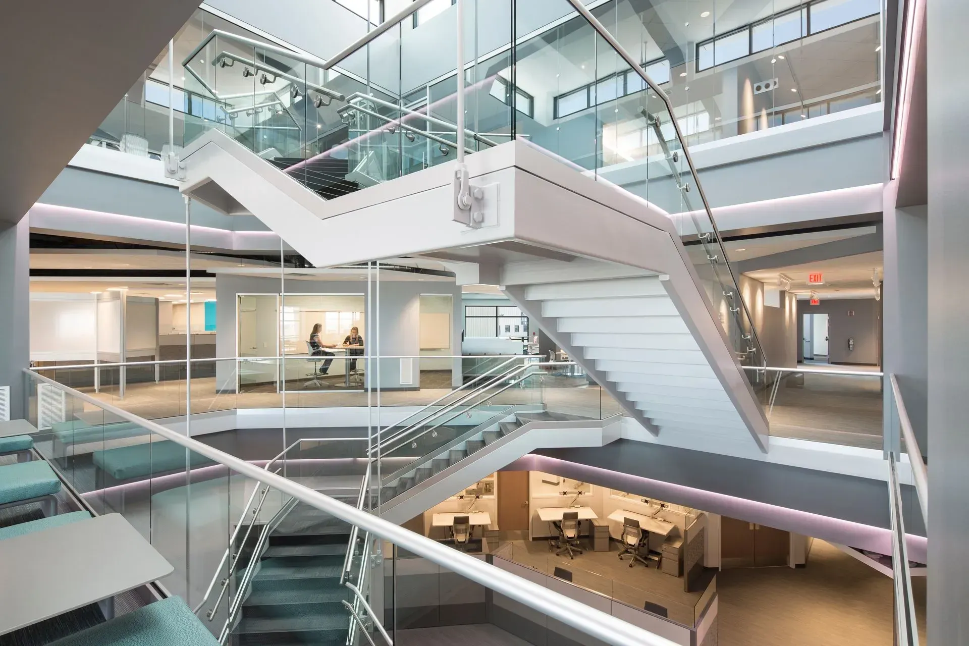 Modern office interior with multiple levels, glass walls, and a white staircase.