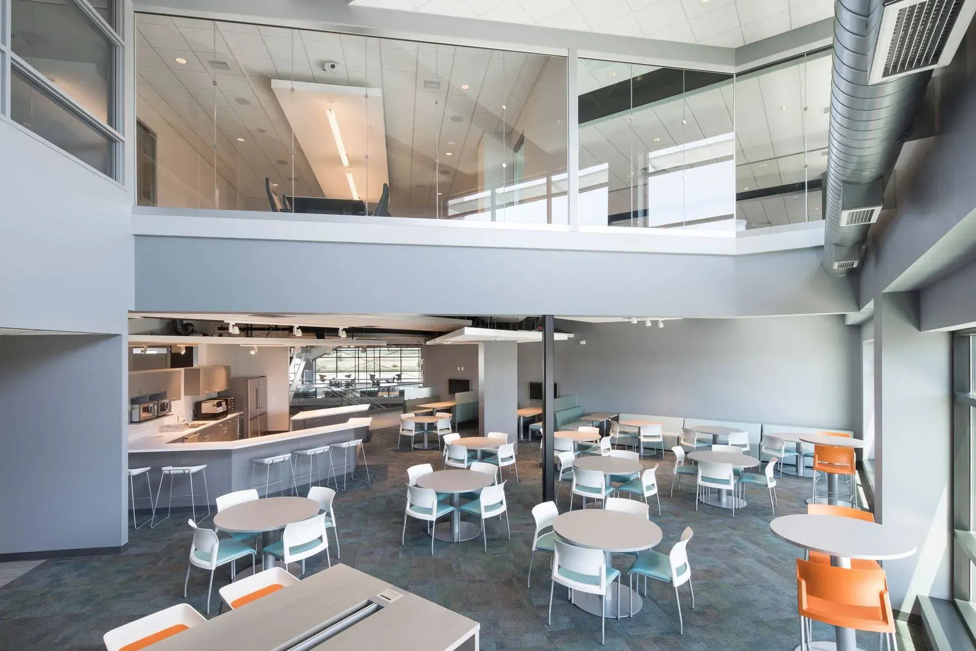 Modern multi-level workspace with gray walls, tables, chairs, and a small kitchen area.