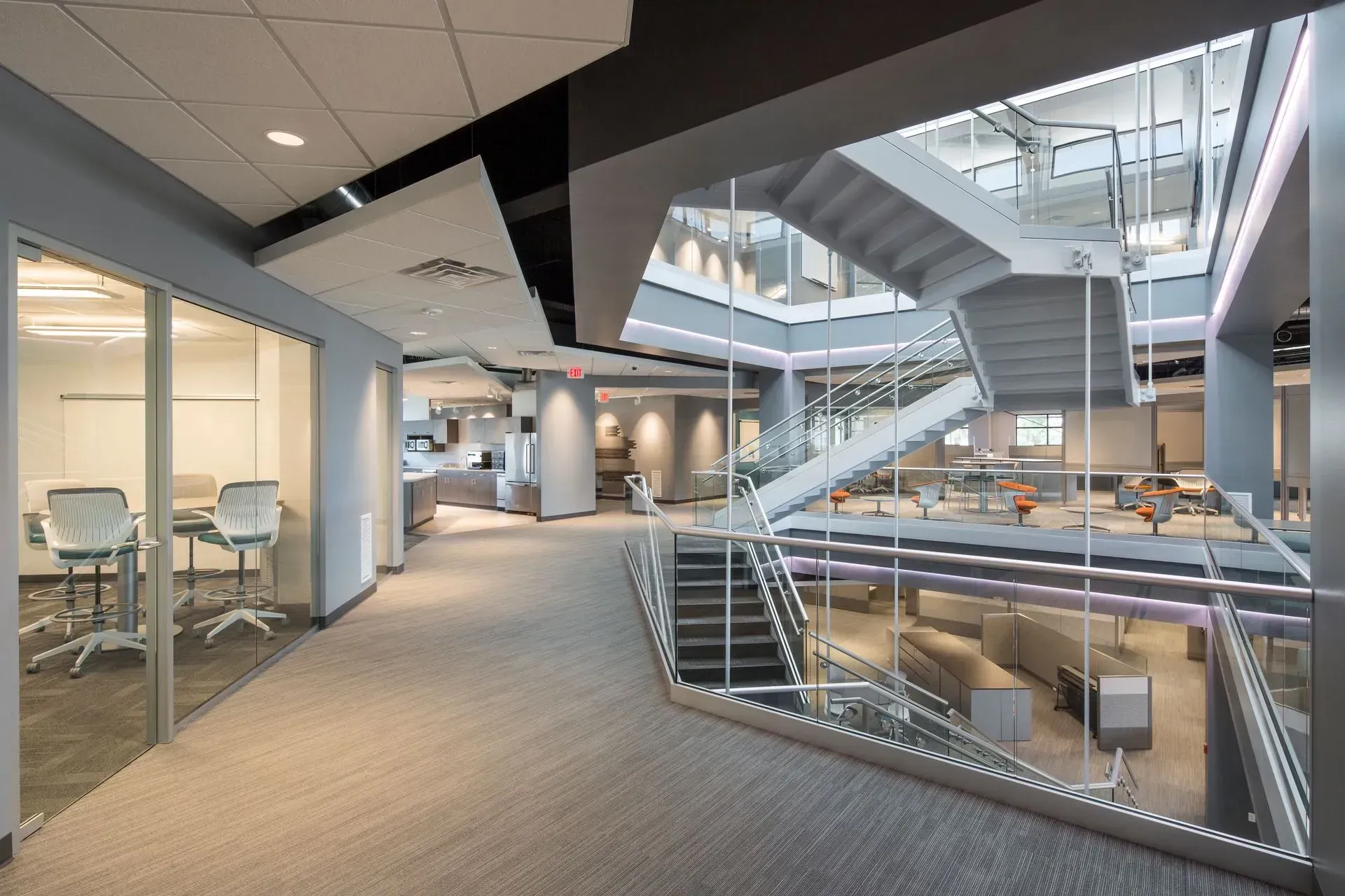 Modern office interior with staircase and glass-walled workspaces. Gray, white, and glass.