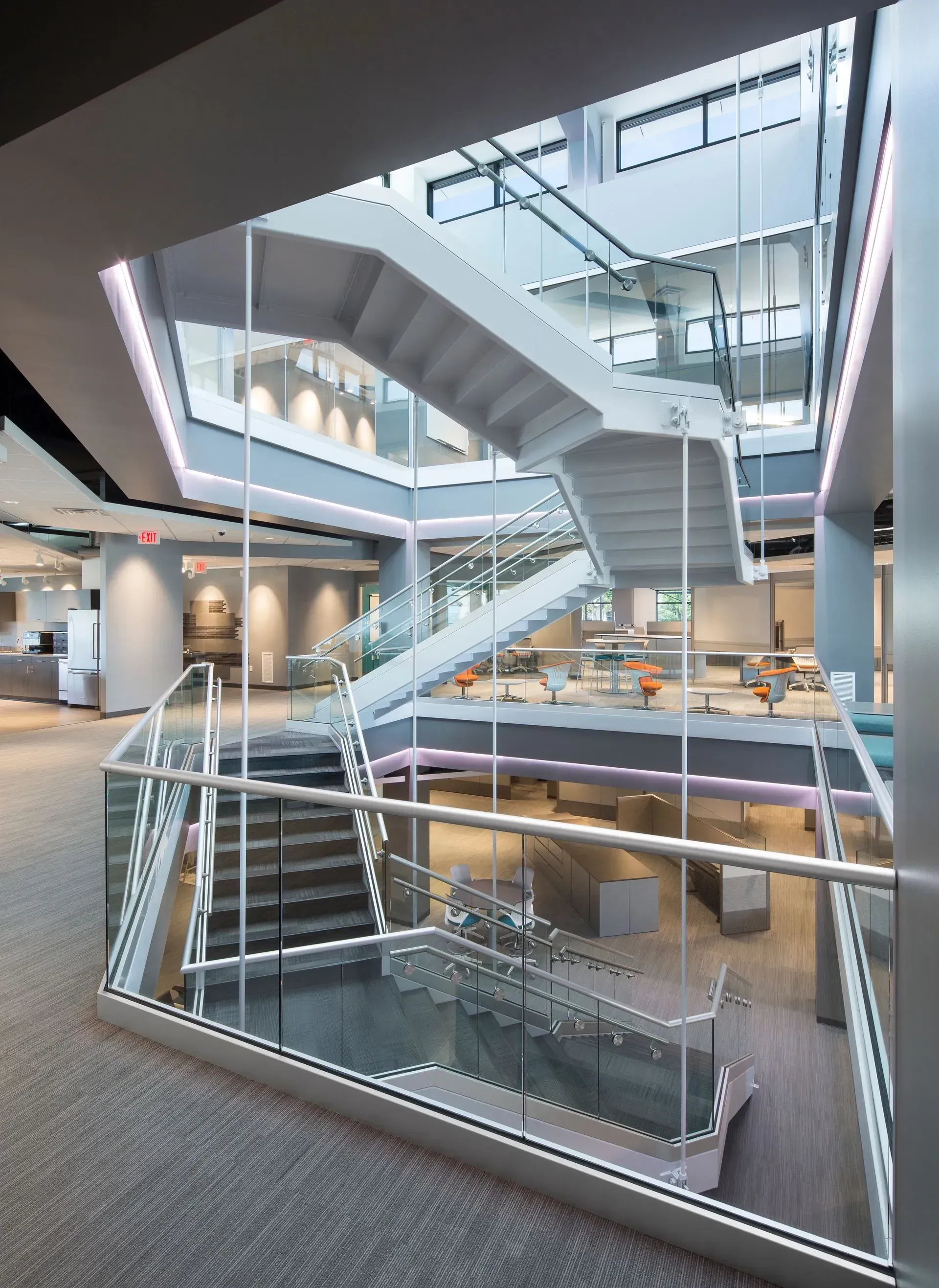 Modern office interior with white staircase, glass railings, and multiple floors.