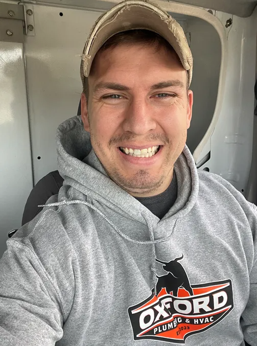 Man wearing Oxford Plumbers & HVAC hoodie and cap, smiling. Inside a vehicle.