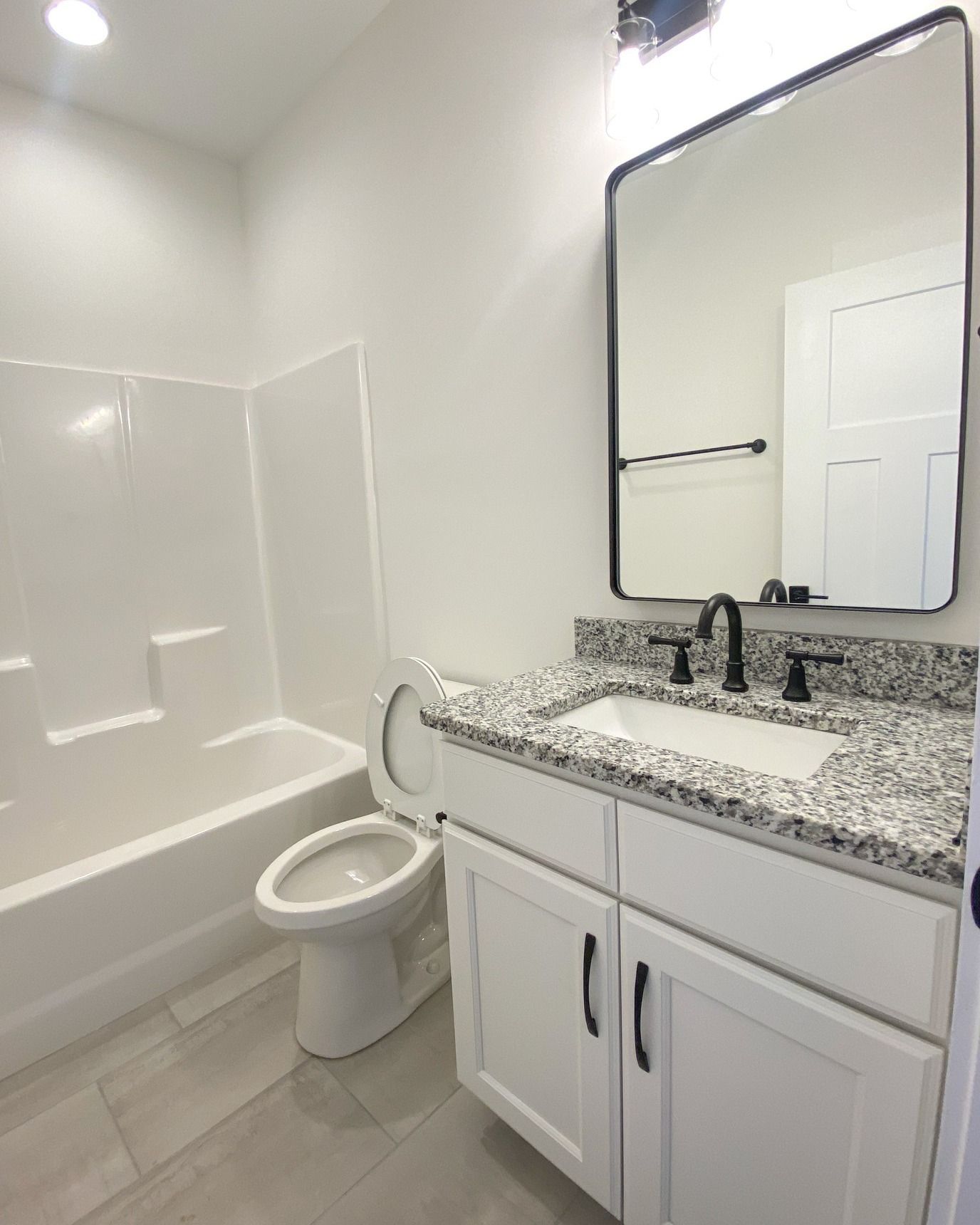 Modern bathroom with black hexagon tile floor, white cabinets, and a large mirror.