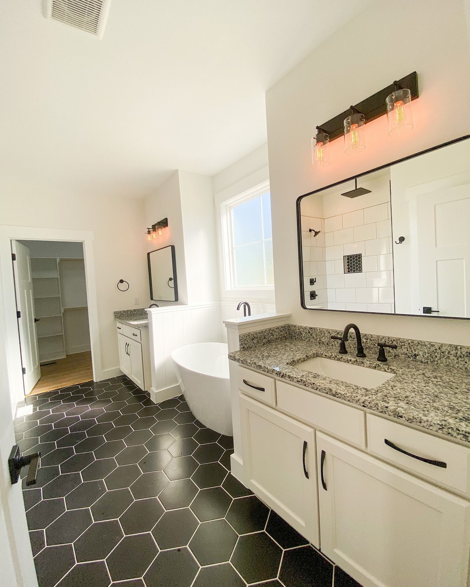 White bathroom with tub, toilet, vanity with granite countertop, and black-framed mirror.