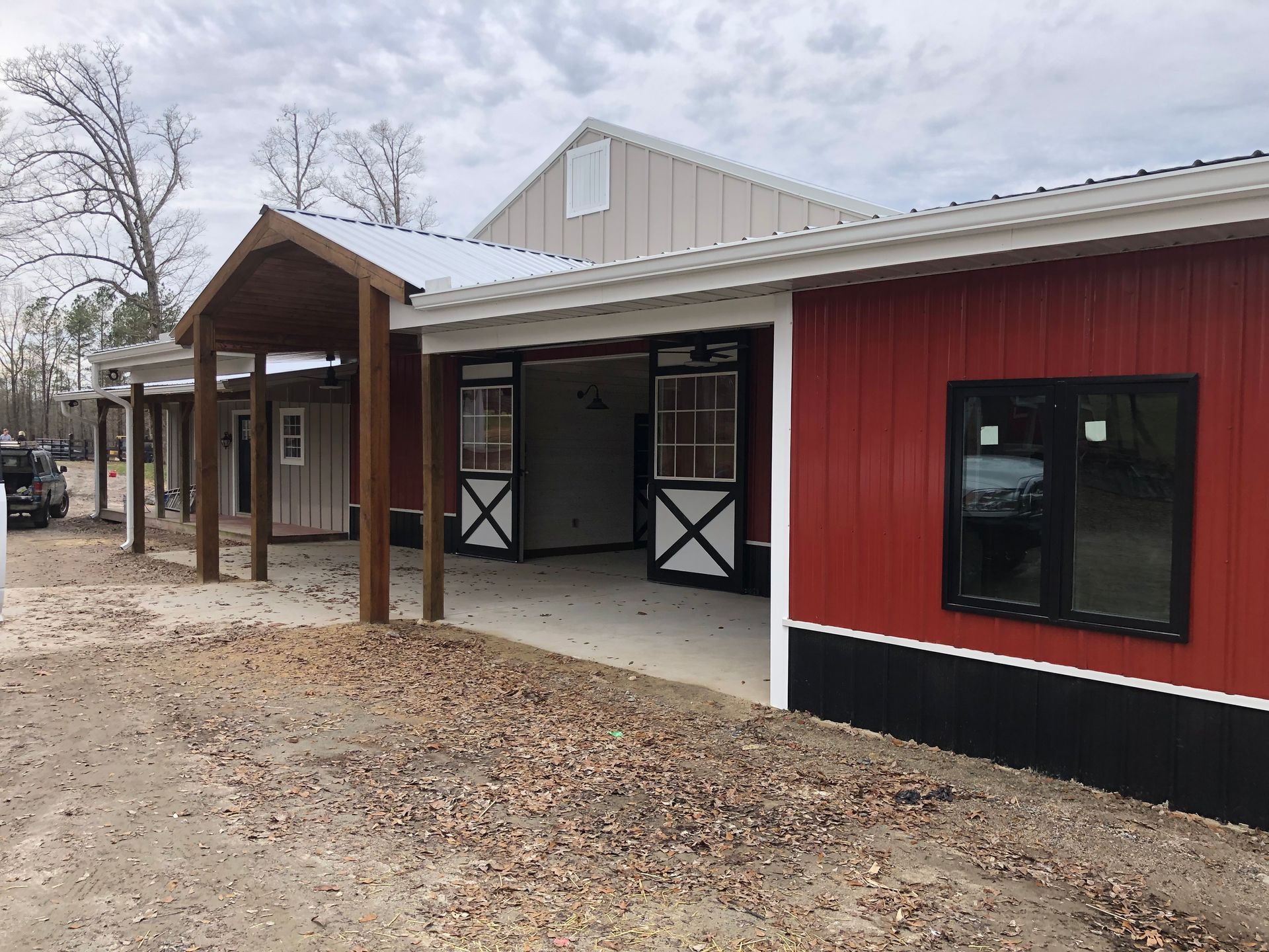 Red barn with open stalls and a covered walkway; overcast sky.