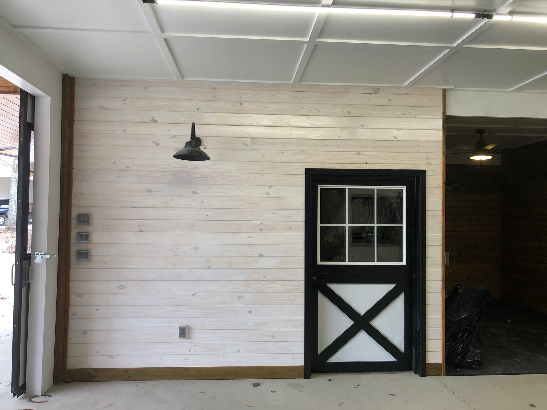 White-washed wood wall with black door and matching light. Open doorway to the left.