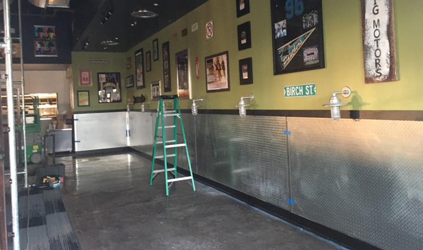 Interior of a restaurant under construction, with metal paneling on the walls, a ladder, and decorations.