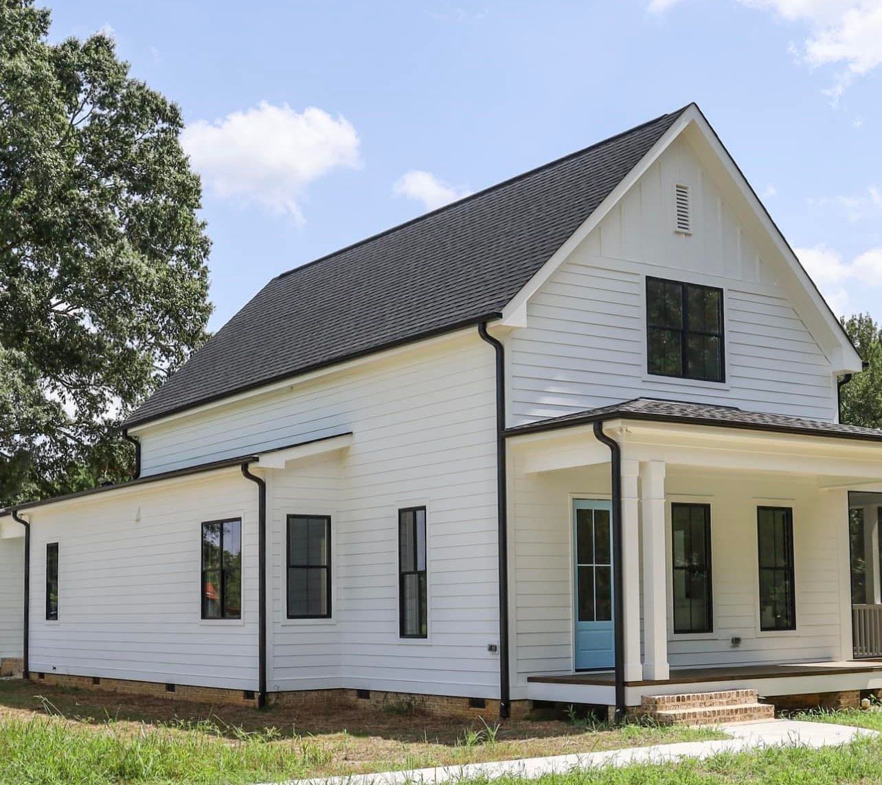 White farmhouse with black trim and roof; blue door; sunny day.