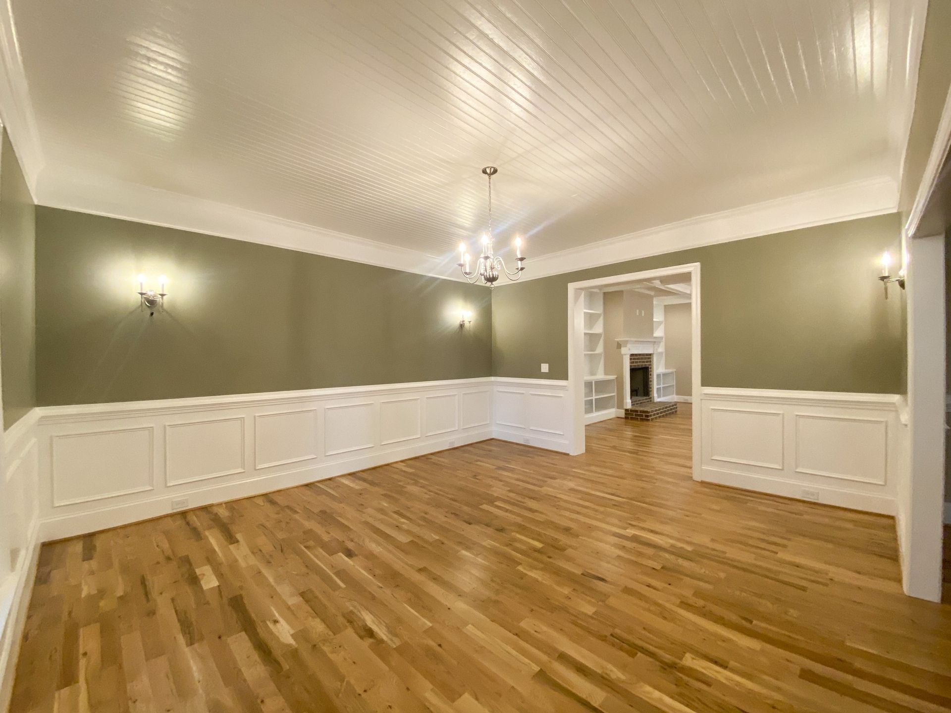 Empty dining room with wood floors, beige walls, white trim, chandelier, and black-framed windows.