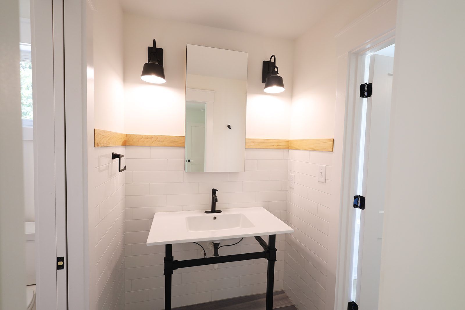 White ranch house with stone accents and a two-car garage, in a wooded area, gravel driveway.