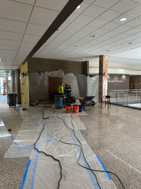 Construction in a building hallway, with workers near a covered wall and protective plastic on the floor.