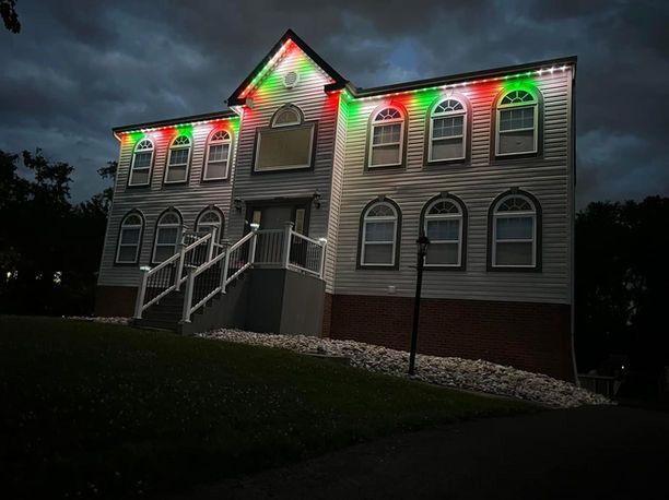 Two-story house lit with red and green holiday lights at night