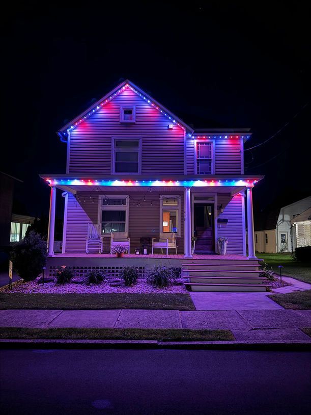 Two-story house lit with purple and blue holiday lights at night