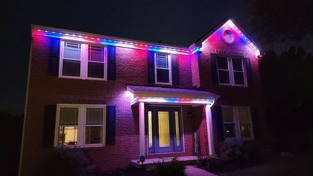 Two-story brick house at night outlined with colorful pink, blue, and white holiday lights