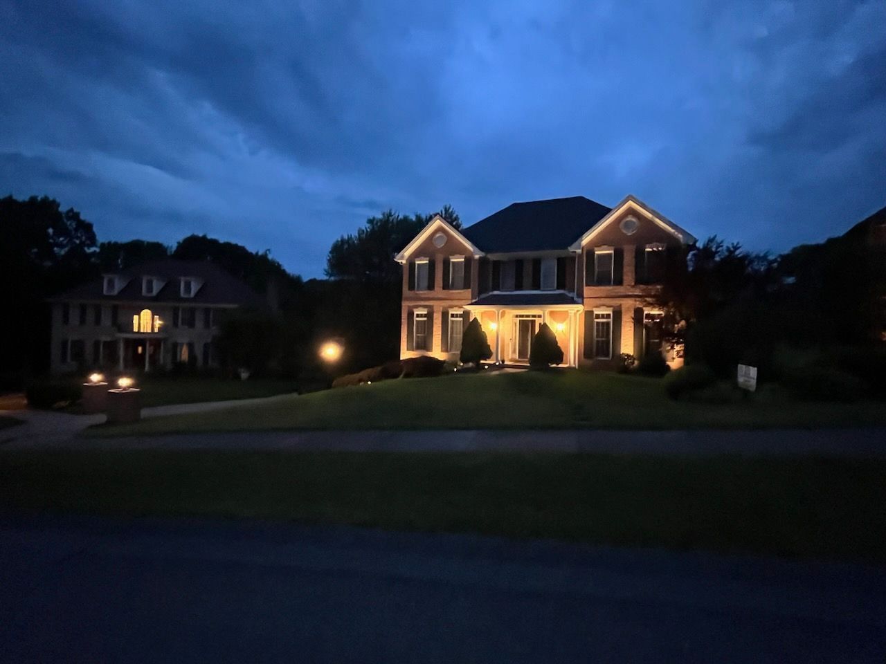 Large suburban house lit warmly at dusk under a dark blue sky