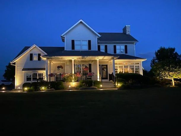 Two-story house at dusk with warm porch lights and a dark lawn in front
