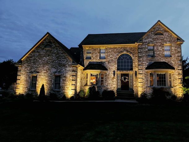 Stone house at dusk, warmly lit exterior with arched windows and dark lawn