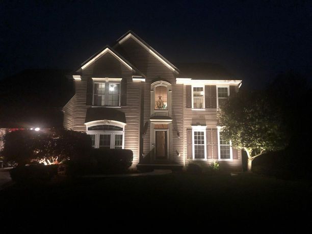 Well-lit suburban house at night with exterior roofline and garden lights