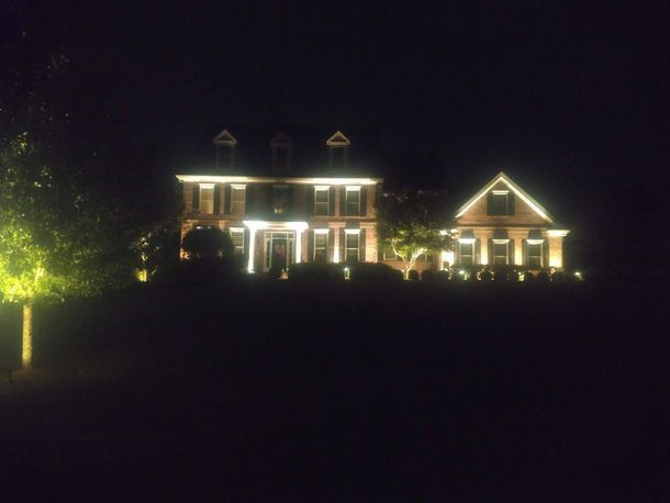 Large illuminated house at night with bright windows and trees against a dark sky