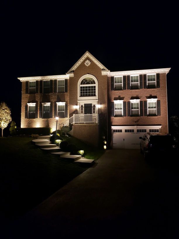 Well-lit brick house at night with dormer windows and a curved front walkway