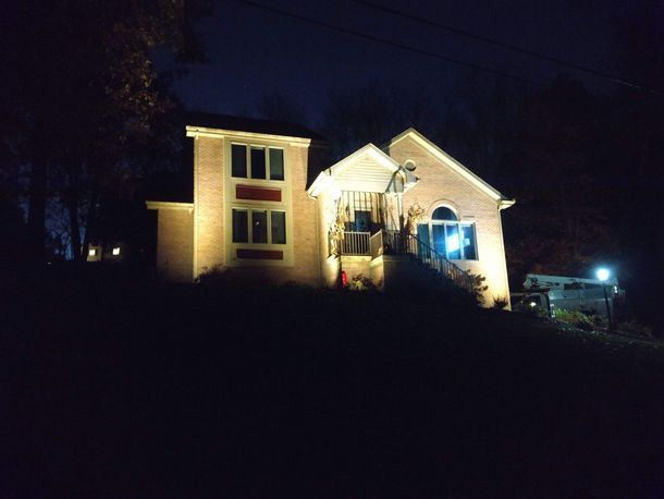 Lit house at night with a front porch and dark yard, viewed from a distance